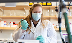 student in white coat and mask working in lab