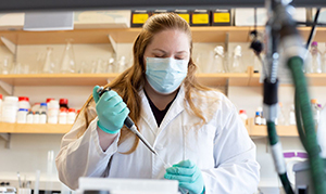 woman with white coat and mask working on experiement