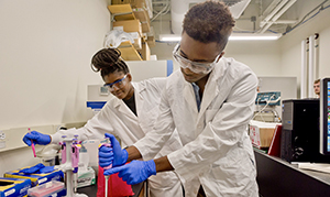 two students in white coats working in a lab
