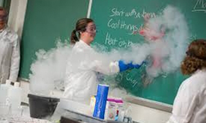 teacher in white coat in lab writing on caulk board