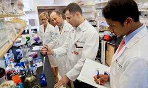 students in white coats all working together in a lab, one student taking notes