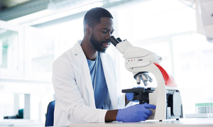 man in white coat looking through a microscope