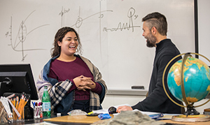 students standing in front of white board with globe on desk beside them