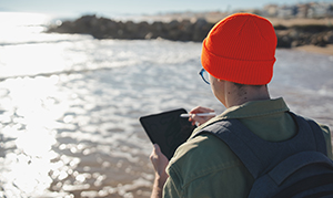 student with ipad taking notes by ocean