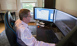 professor sitting at desk looking at multiple desktop screens