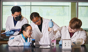four students in lab coats working on an experiment in a lab