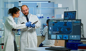 two people looking at information on clipboard with medical technology behind them