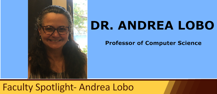 An headshot of Dr. Andrea Lobo standing in her office. She is lit by a window in the background, and is smiling. 