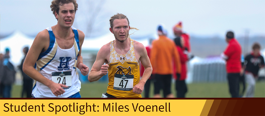 An image of Miles Voenell in the middle of a race. The sky is cloudly, and there is a white man in a blue running uniform on his right. On his right, there is a yellow, slightly opaque square that reads, "Student Spotlight: Miles Voenell".