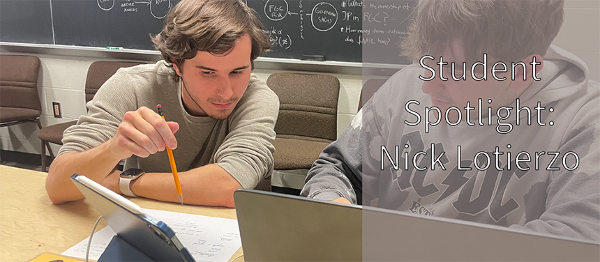 A photograph of Nick Lotierzo tutoring a student. Both men are seated at a blonde wooden table in the CS drop-in tutoring room. There is a blackboard with various equations behind them, as well as brown, felt chairs lined up in a row against the beige wall. Nick is a young white man, wearing a long sleeved gray shirt pushed up to his elbows. He has brown hair swept to either side of his face. He has a thin brown beard. He’s pointing with a pencil at a tablet screen. The tablet is blue, with an electronic pen resting on top. The tutee is another white young man, with a partial beard and dirty blonde hair. He is wearing a gray AC/DC sweatshirt. He is looking to where Nick is pointing. On the table, you can see the top quarter of his silver laptop. At the bottom right of the screen is a slightly opaque gray square that reads: Student Spotlight: Nick Lotierzo. 