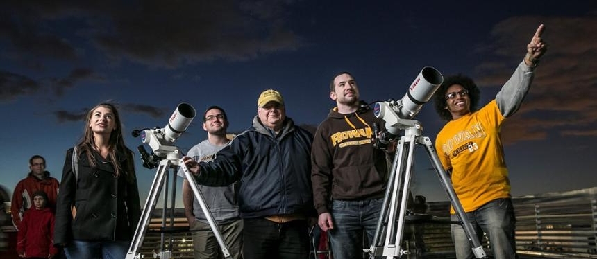 students outside at night looking up next to telescope