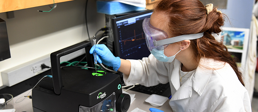 student in white coat and goggles conducting research