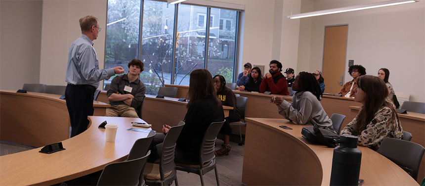 A photograph of Micheal Meyer talking with students in a Buisness Hall lecture room.