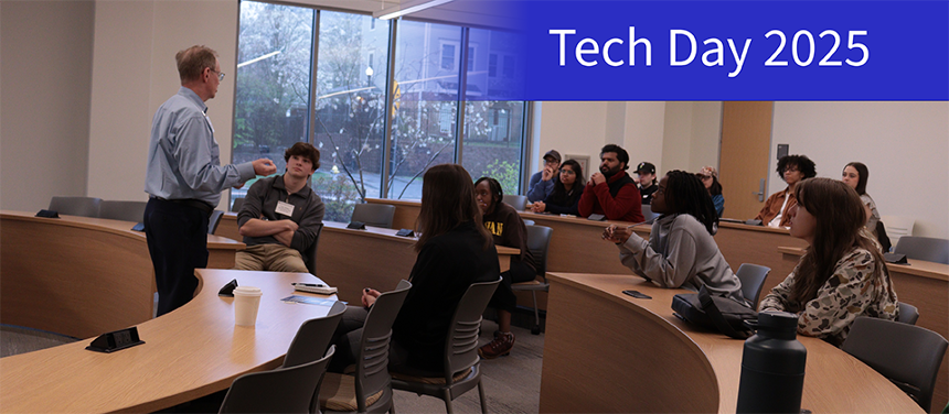 A photograph of Micheal Meyer talking with students in a Buisness Hall lecture room. In the top right corner is a navy blue rectangle that becomes transparent as it moves left across the screen. On the navy blue banner is white text that reads, "Tech Day 2025."