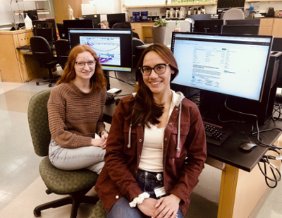 two students smiling in front of a computer