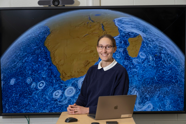 Helga Huntley sitting behind laptop with ocean map behind