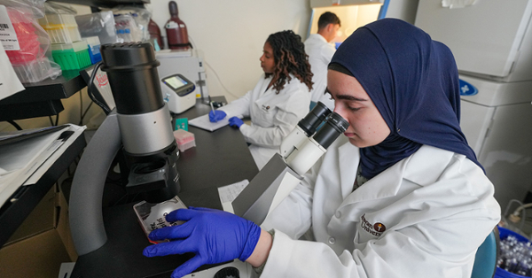 Fatima Akin wearing protective gloves and a lab coat working in virologist lab